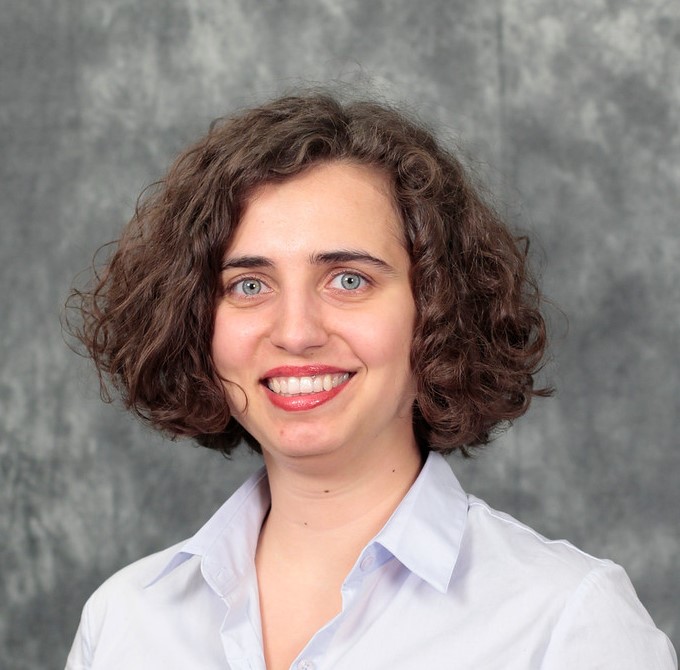 A headshot of a woman with curly, short, ear-length hair with green eyes and red lipstick.